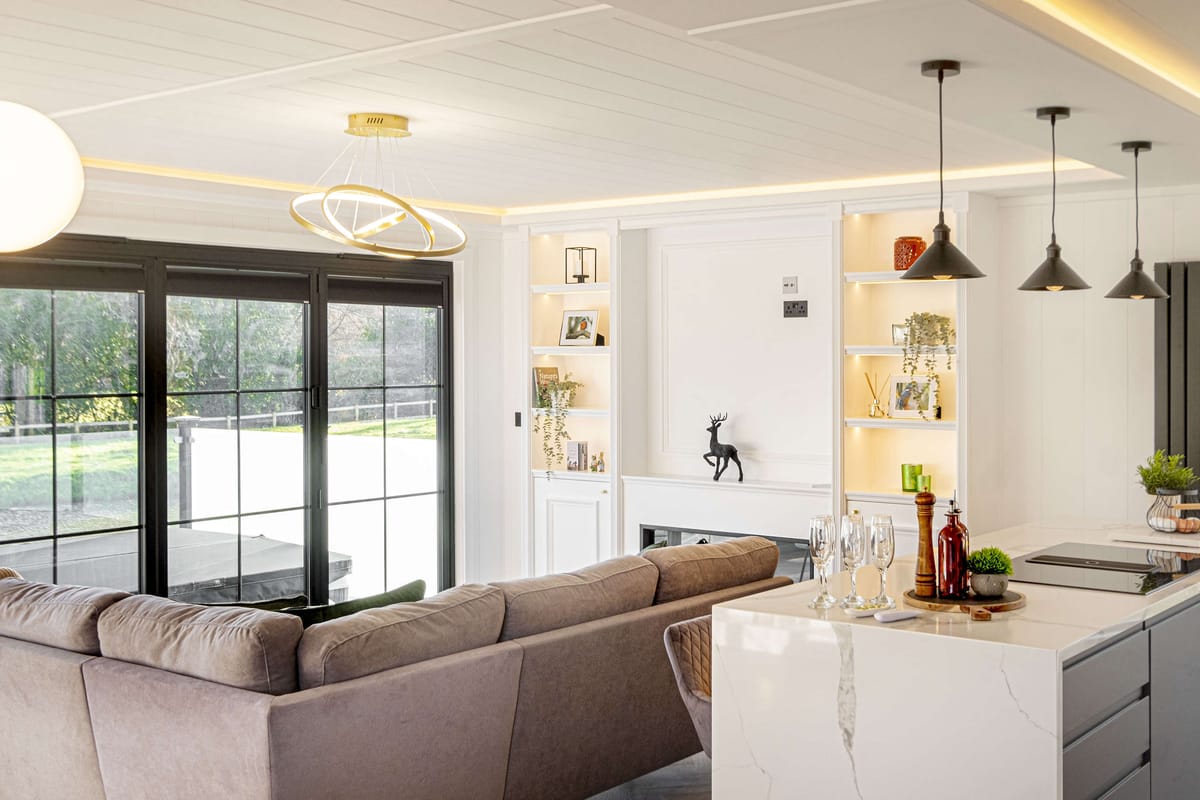 Modern Open-Concept Living Room with Cozy Sectional Sofa, Elegant Marble Countertop Island, and Stylish Pendant Lighting in a Bright, Sunlit Space Featuring Large Windows and Tasteful Decorative Accents