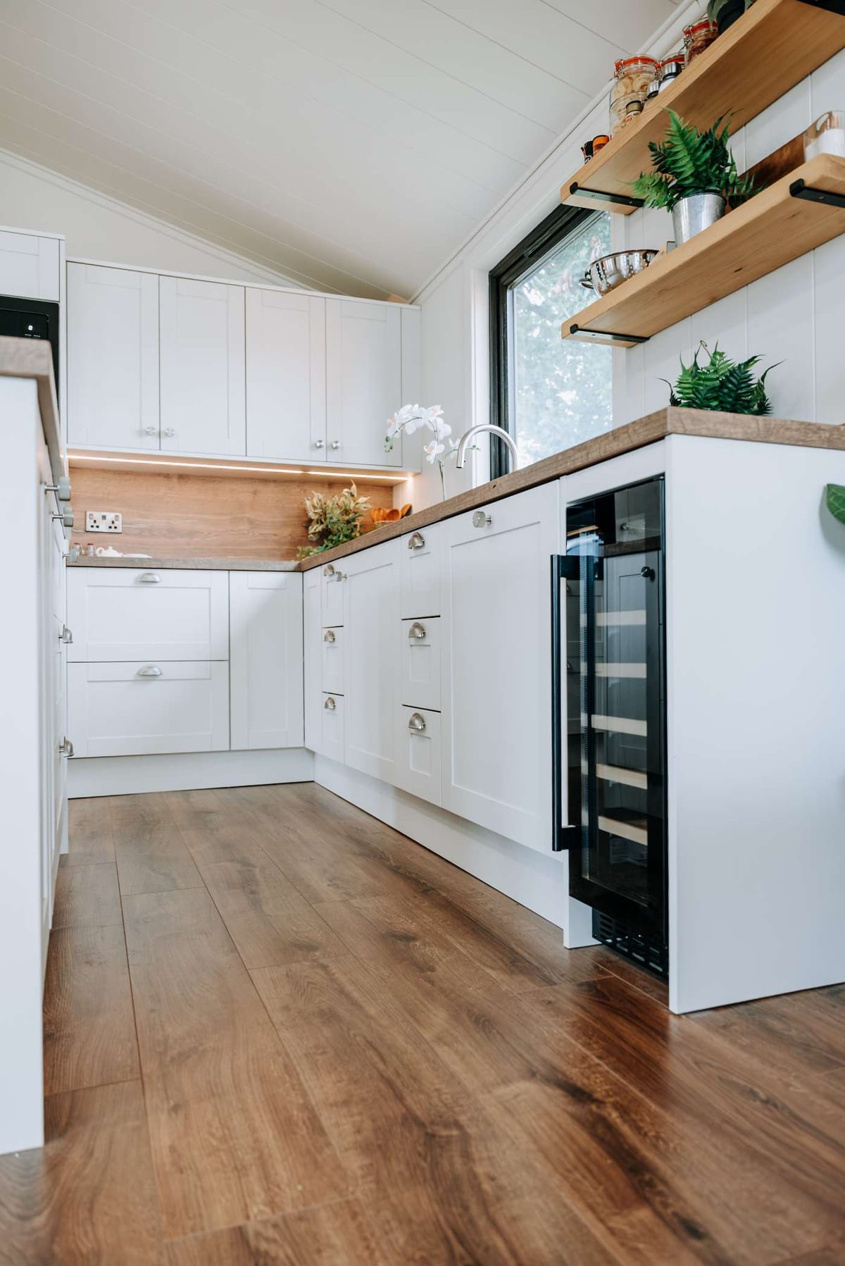 Modern Kitchen Interior with White Cabinets, Wooden Flooring, and Open Shelving Featuring Plants and Decorative Items