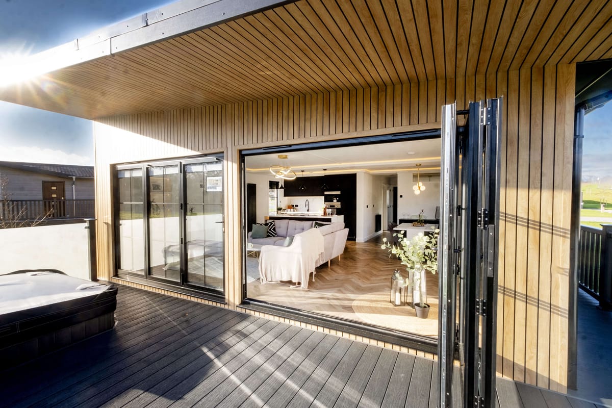 Contemporary Wooden Terrace with Glass Doors Leading to Modern Open-Plan Living Room and Kitchen Featuring Elegant Lighting and Decor Elements