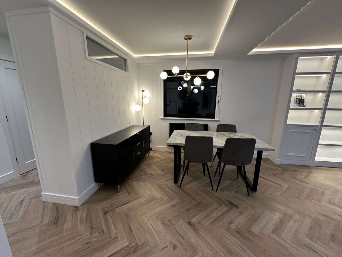 Modern Dining Area with Herringbone Wood Flooring, White Paneled Walls, Minimalist Black Sideboard, Contemporary Lighting, and Built-in Display Shelves