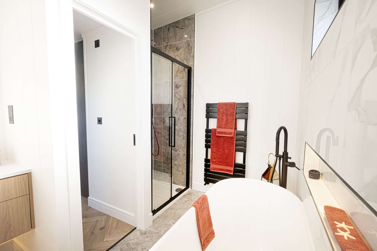 Modern Bathroom Interior with Freestanding Bathtub, Glass-Enclosed Shower, Black Towel Rack with Red Towels, and Wood Accents on Vanity in Brightly Lit Space
