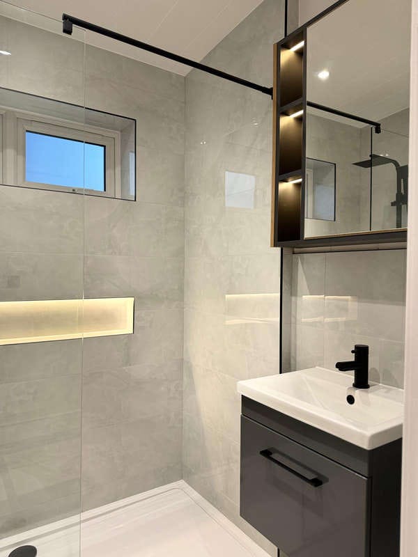Modern Minimalist Bathroom with Glass Shower Enclosure, Sleek Black Fixtures, Illuminated Recessed Shelf, and Compact Vanity Unit with Mirror Cabinet