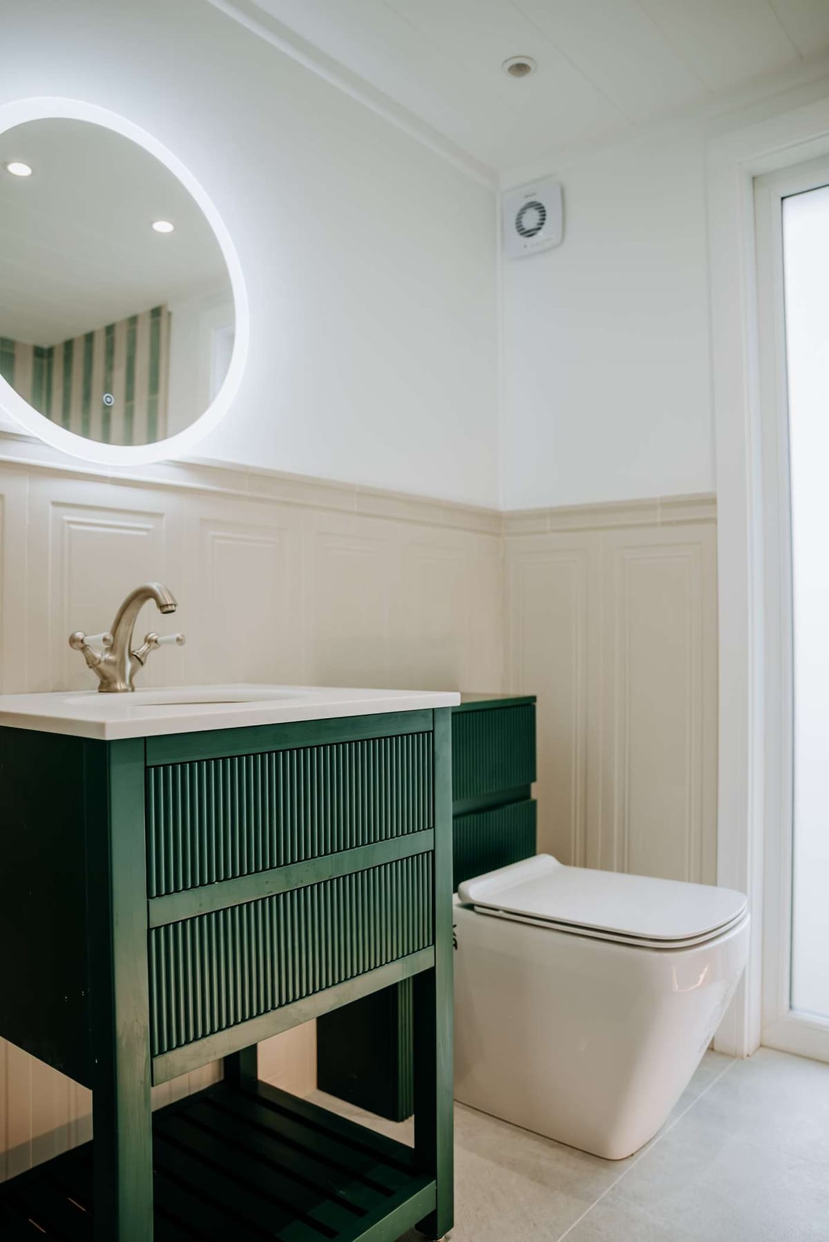 Modern Bathroom Interior with Illuminated Circular Mirror, Elegant Green Vanity, and Sleek White Toilet in Minimalistic Design Setting