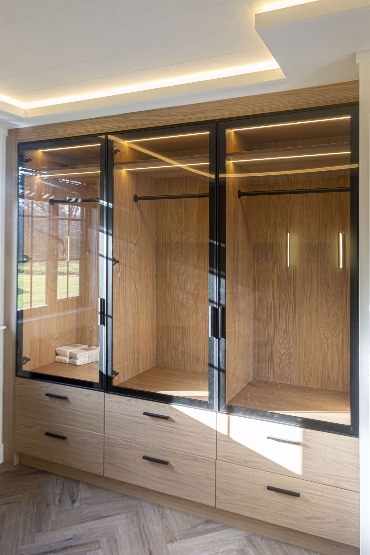 Sleek Modern Wardrobe with Glass Doors, Wooden Interior, and Integrated LED Lighting in Sunlit Room