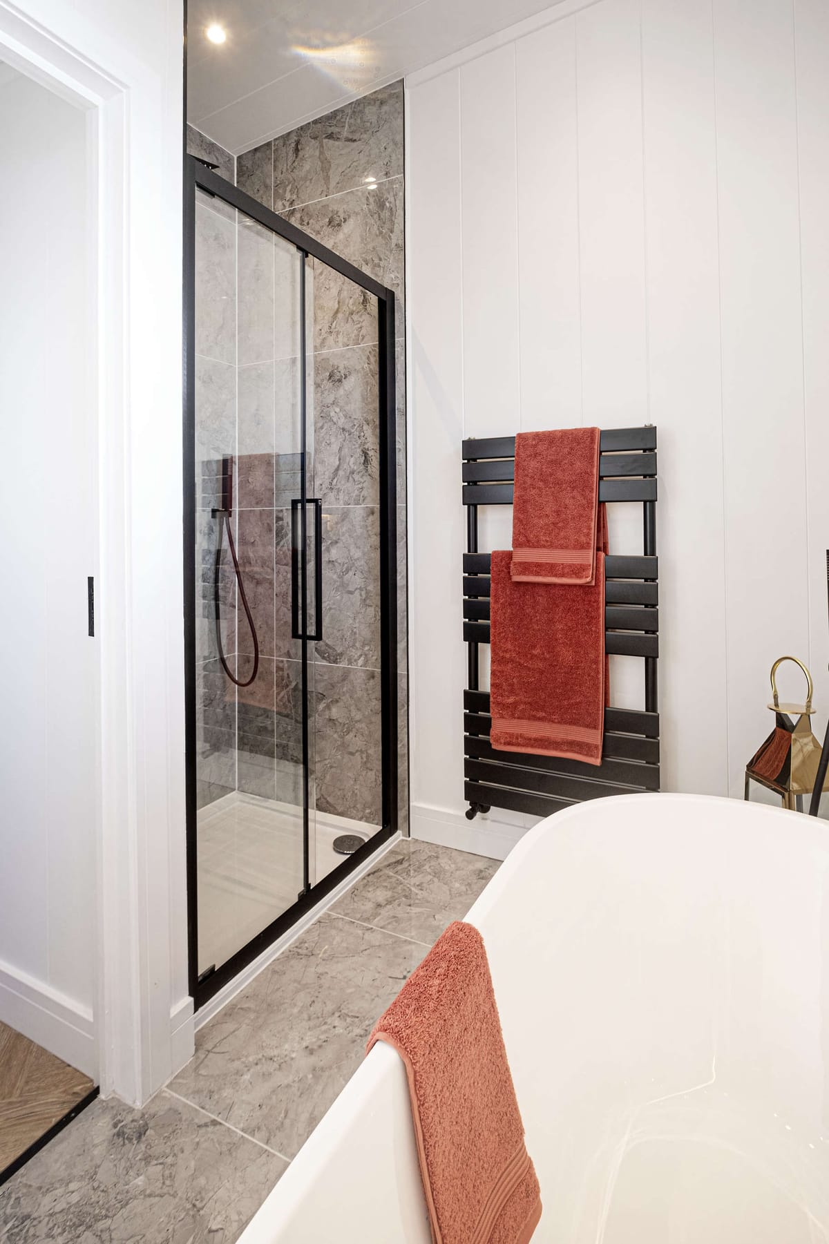 Modern Bathroom with Glass-Enclosed Shower, Freestanding Tub, and Coral Towel Accents on Black Heated Towel Rack