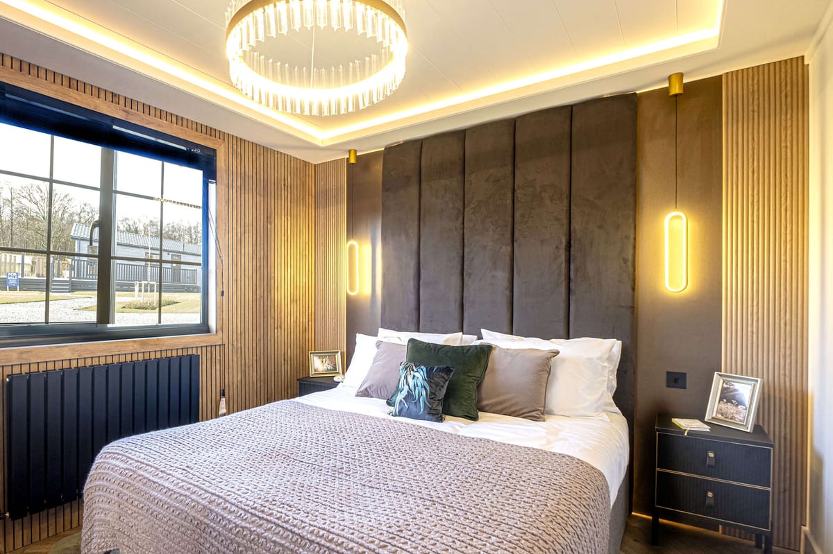 Luxurious Contemporary Bedroom Featuring a Plush Bed with Layered Cushions and a Textured Blanket, Elegant Vertical Paneling, Modern Pendant Lighting, and a Large Window with Outdoor View, Enhanced by a Stylish Chandelier and Minimalist Nightstands.