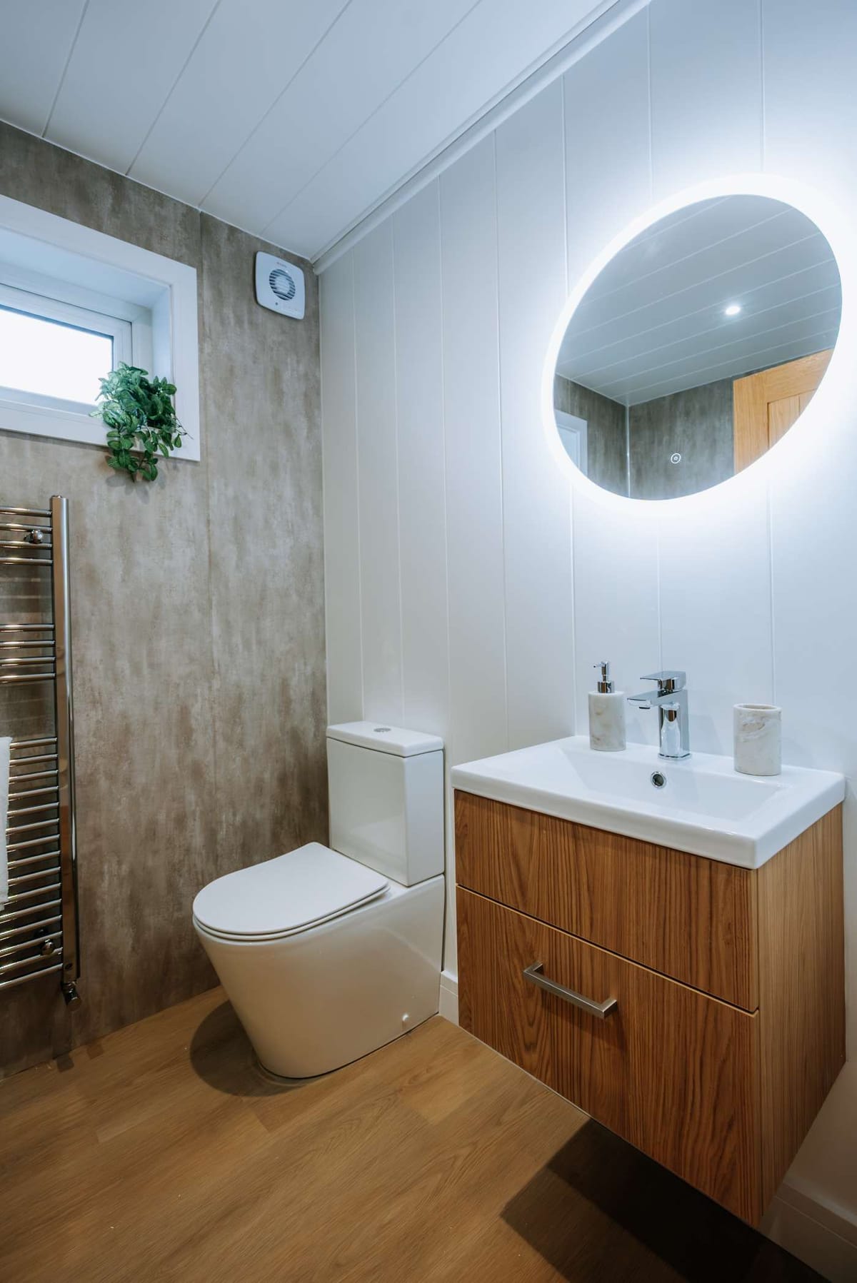 Modern bathroom with a wooden vanity, illuminated round mirror and wall-mounted towel rack