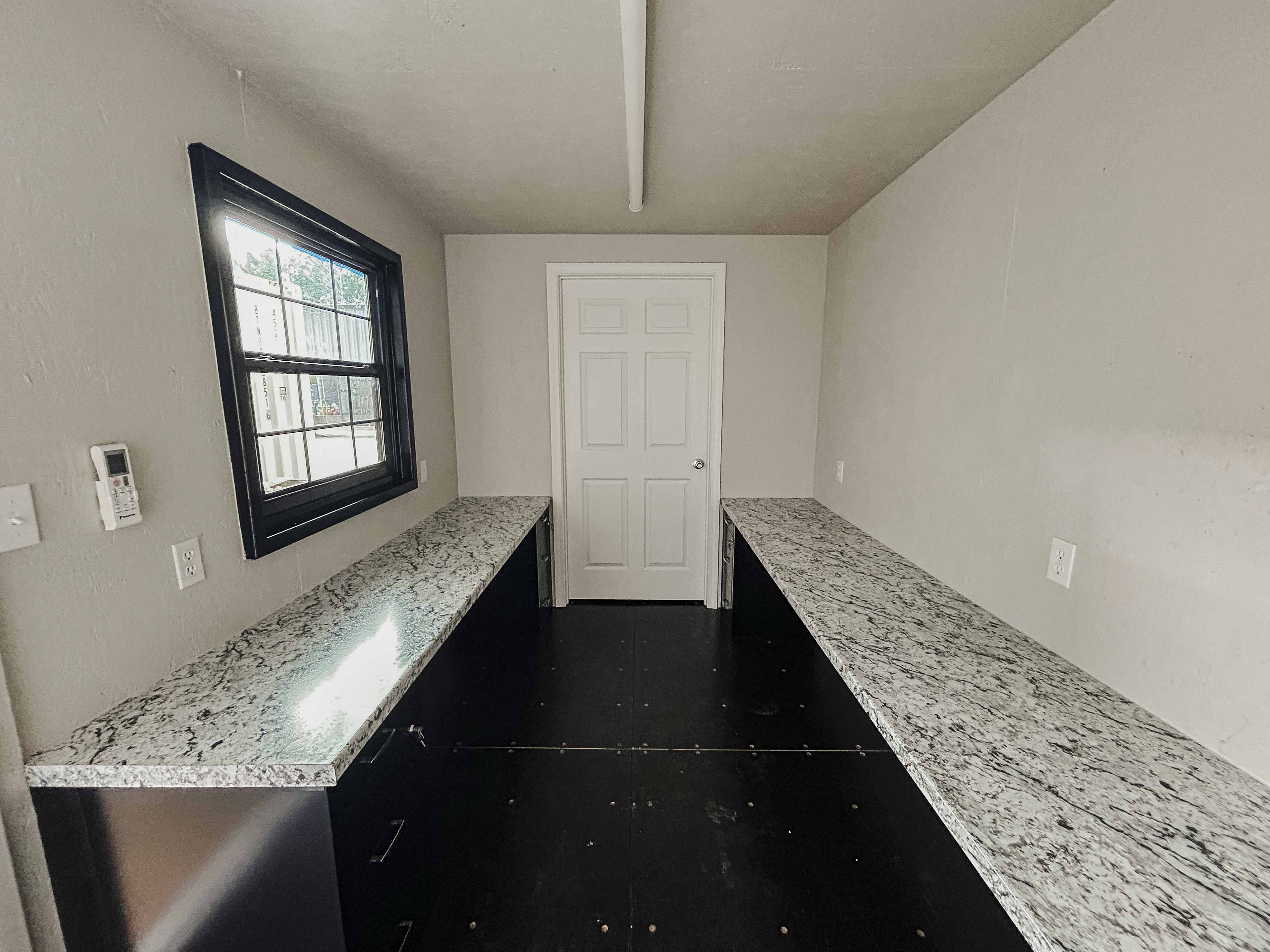 20-foot custom container office interior with dual granite-look work counters, climate control, a black-framed window, and clean light-gray wall finish—ideal for jobsite offices or mobile workspaces