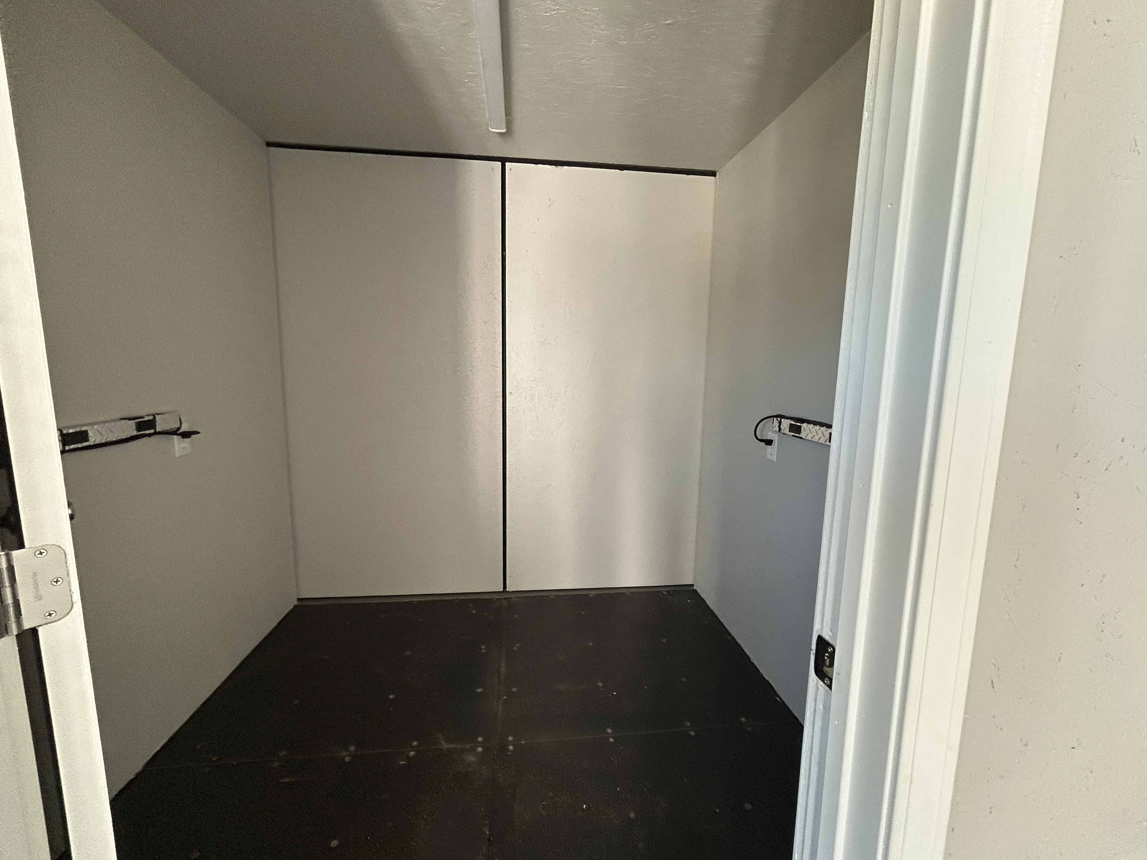 Interior of a custom-built shipping container showing a clean, insulated storage room with finished walls, mounted shelving brackets, and a durable dark flooring system.