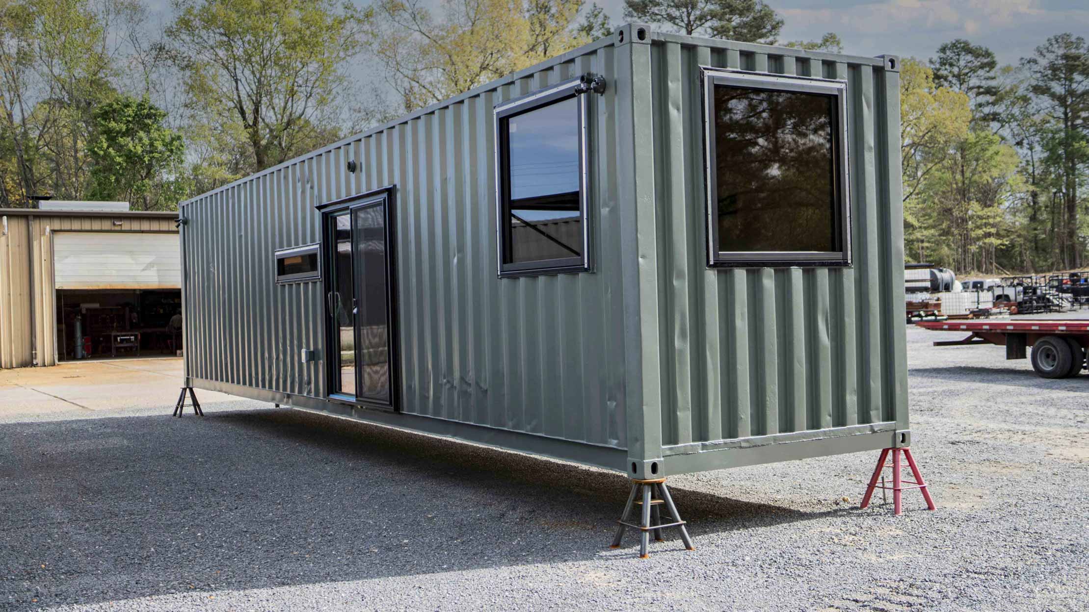 Exterior of custom shipping container hunting cabin featuring large insulated windows, sliding glass door, and military-green finish—fully converted container home ready for transport.