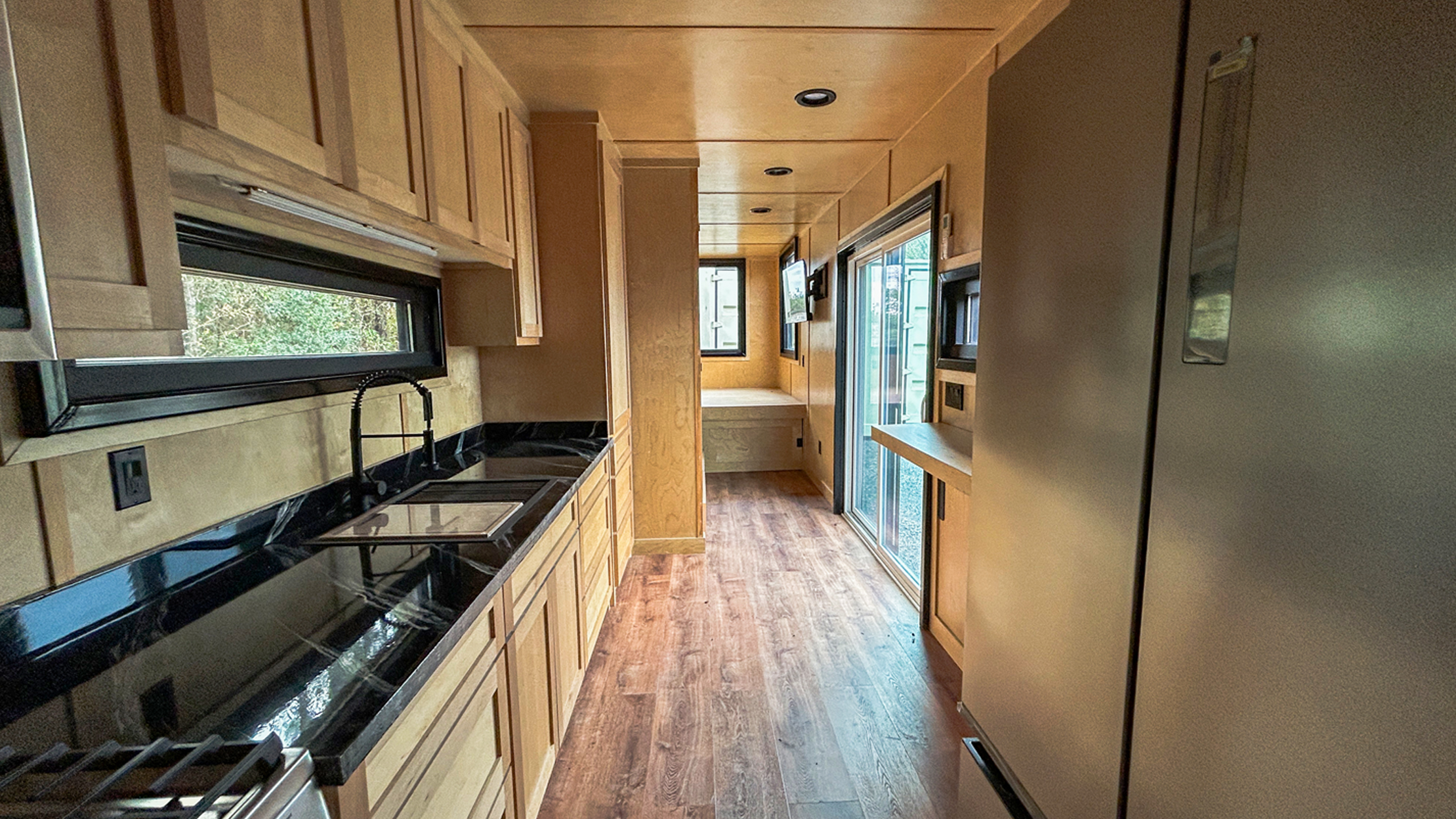 Custom hunting cabin container kitchen with full cabinetry, black countertops, stainless steel appliances, and panoramic window—premium off-grid container home design.