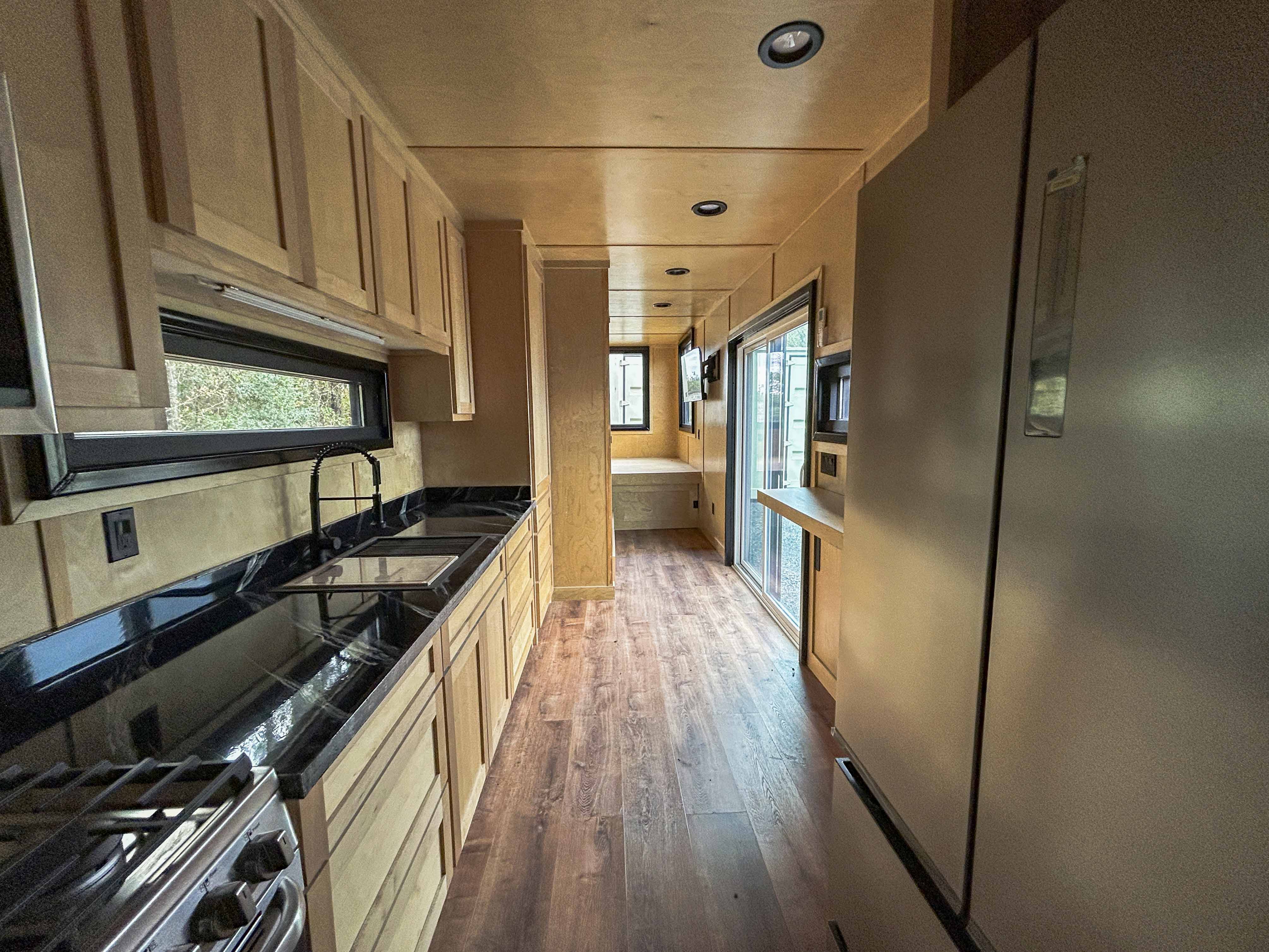 Custom hunting cabin container kitchen with full cabinetry, black countertops, stainless steel appliances, and panoramic window—premium off-grid container home design.