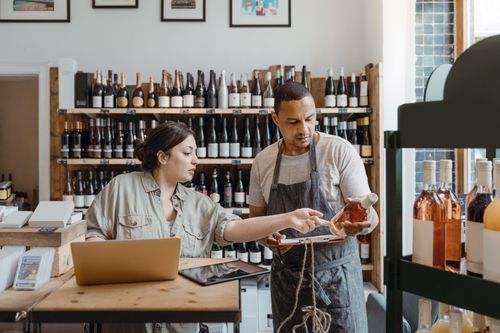 A pair of retailers is checking if a bottle they took from the shelf matches the one ordered by an online customer.