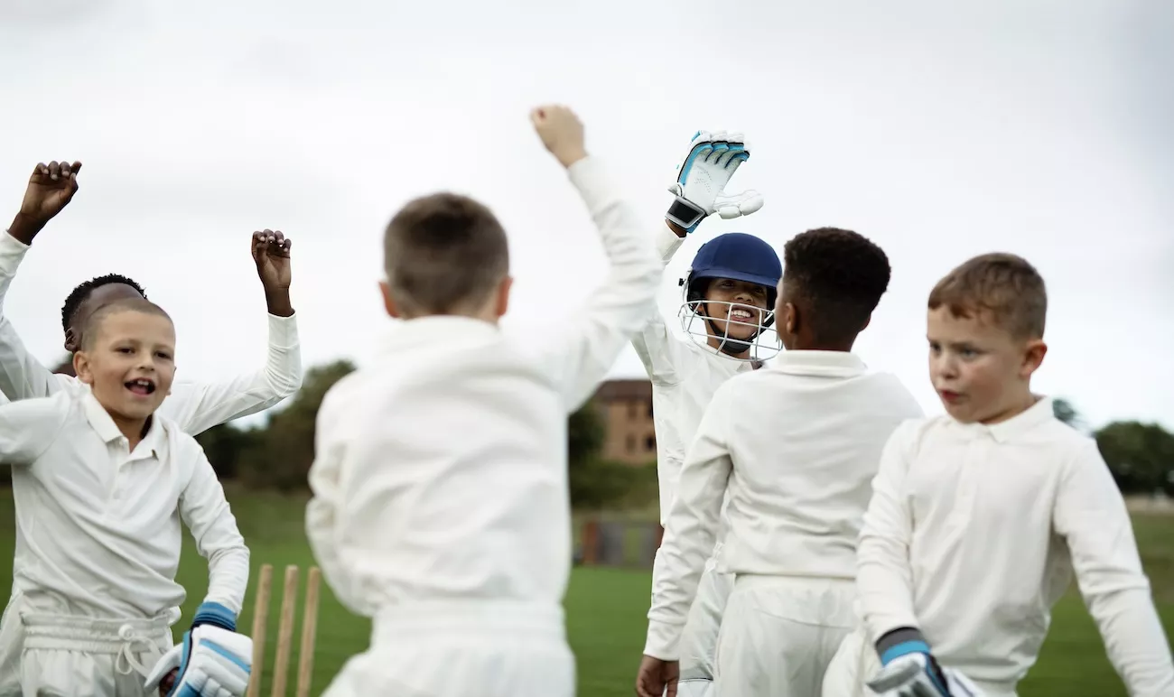 Young cricketers in whites celebrating together on a pitch at a children's hardball cricket holiday camp