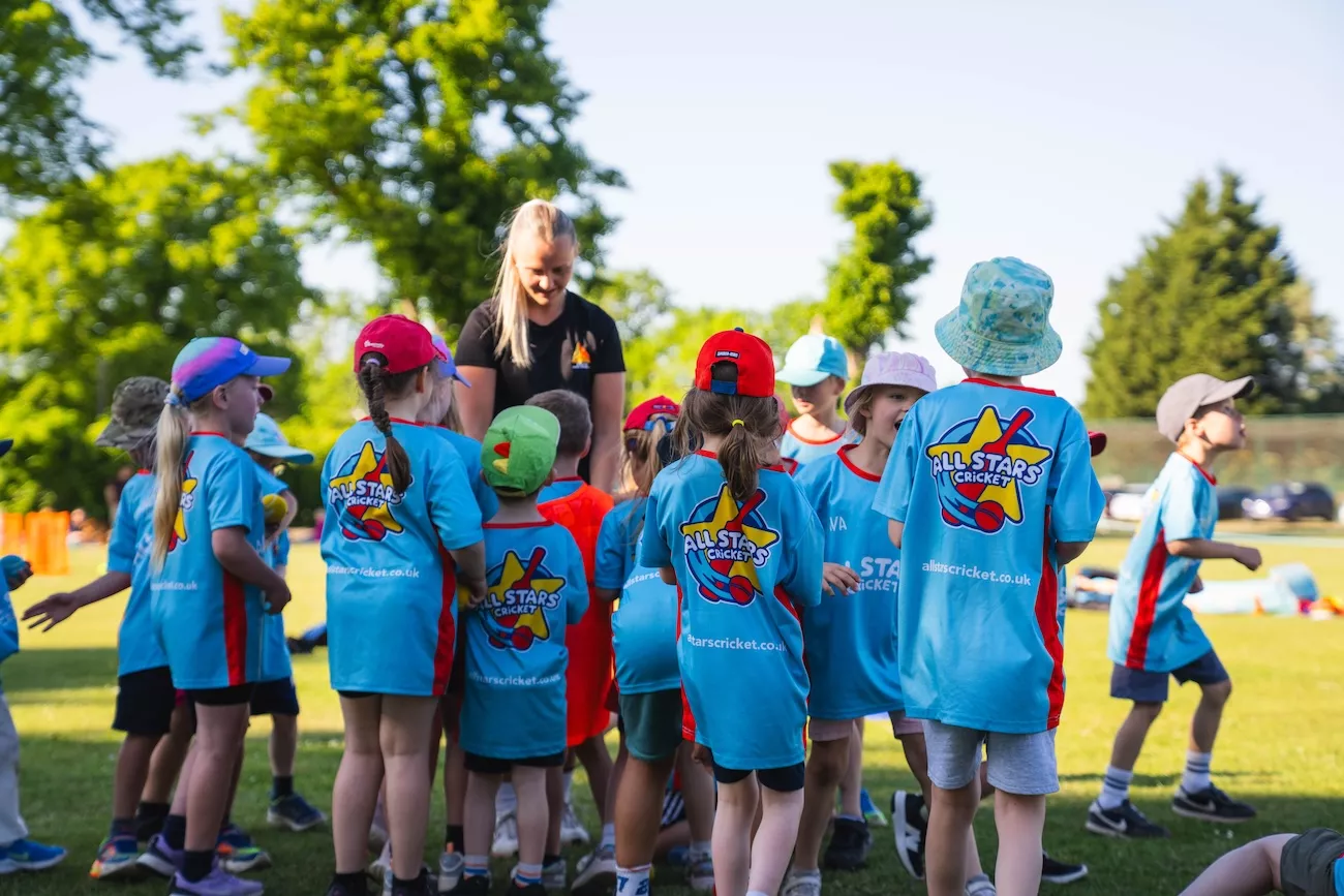 Children in All Stars Cricket t-shirts gather round their coach during a session with Delta Sports Coaching in Worcester.