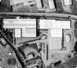 Visão aérea em preto e branco de um grande complexo industrial com vários edifícios e estacionamento.