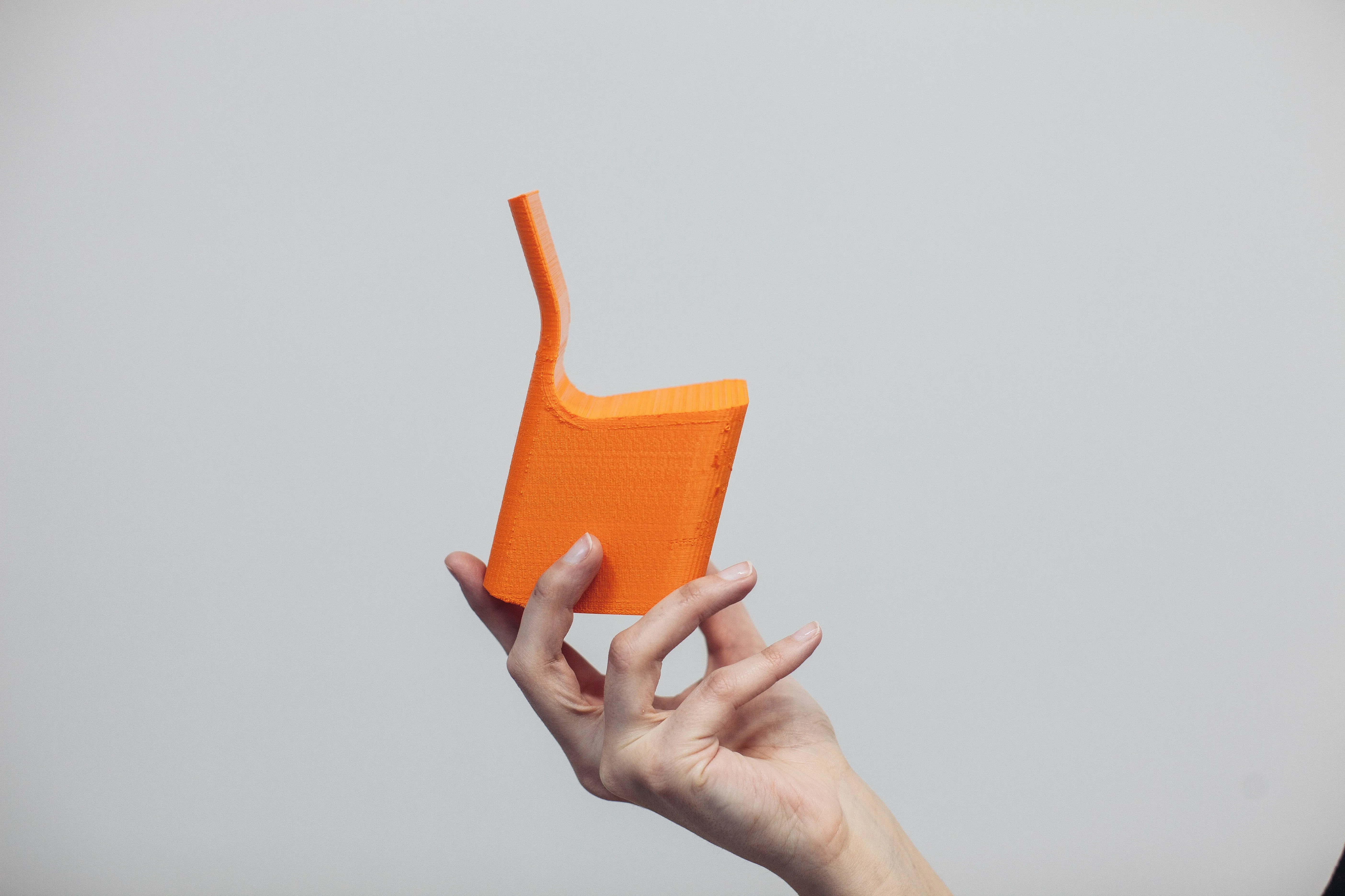 Mão segurando uma pequena cadeira laranja de design moderno contra fundo cinza.