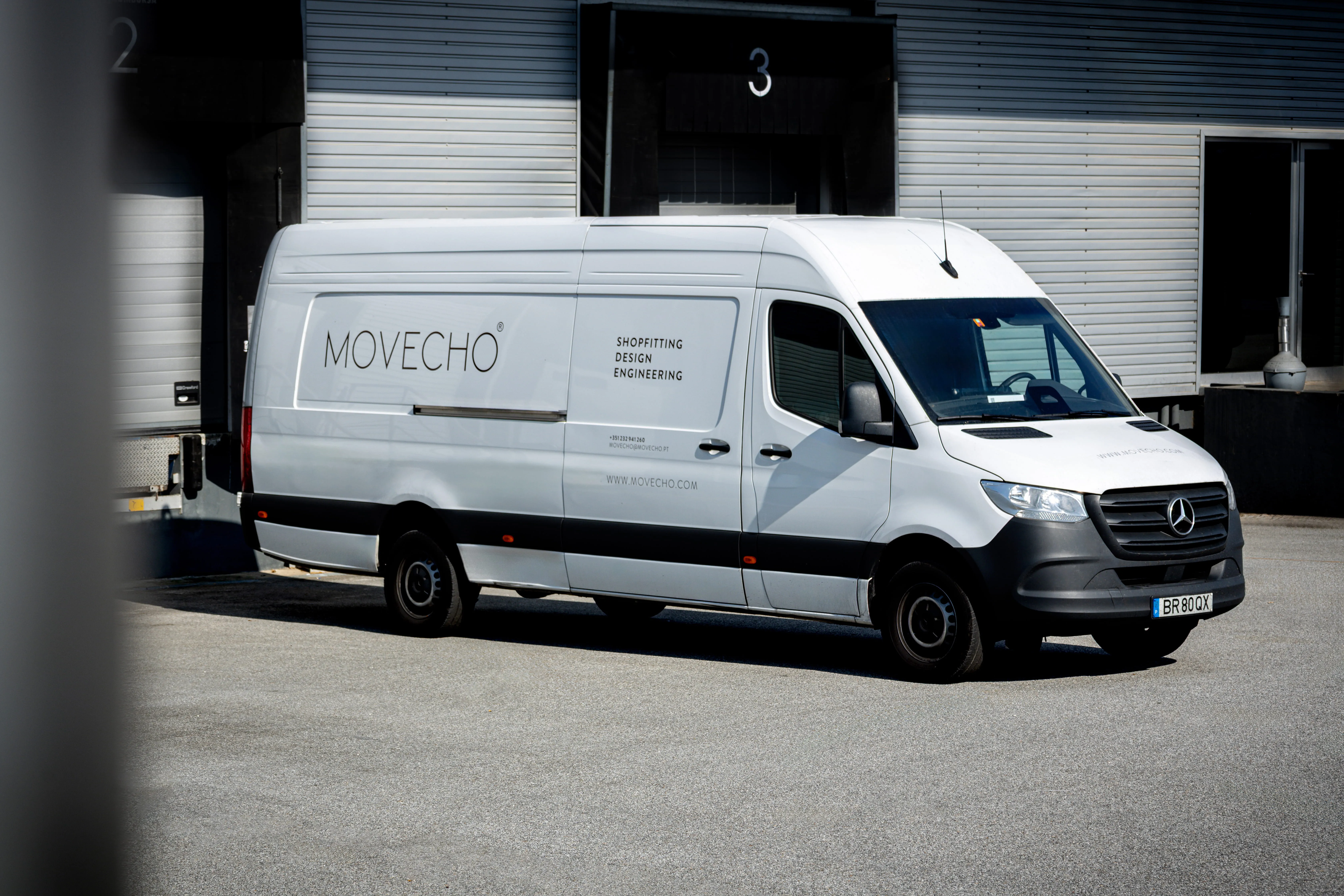 Van branca Mercedes-Benz estacionada ao lado de um armazém com texto Movecho e informações de design.