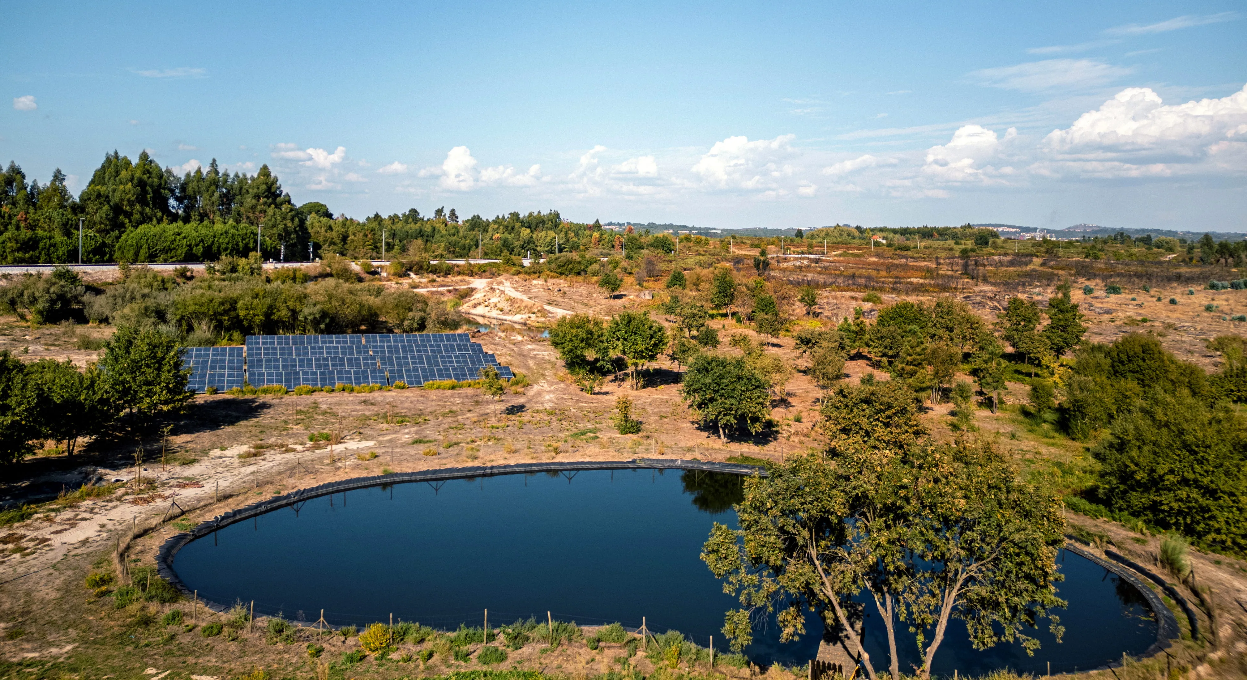 Tanque de água redondo ao ar livre com painéis solares ao lado em área rural com árvores e céu azul.