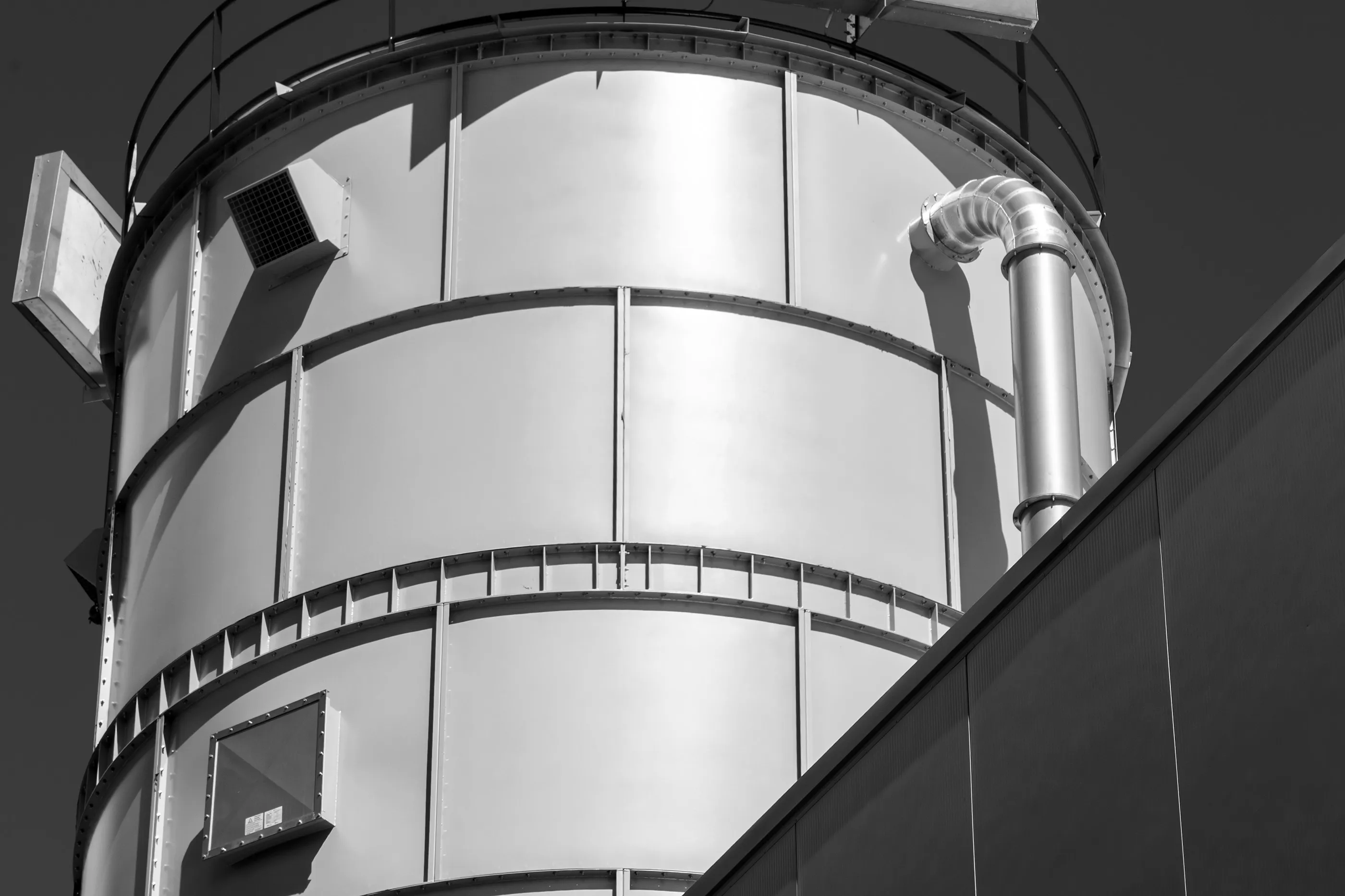 Estrutura industrial metálica cilíndrica com tubulação e paredes externas escuras.
