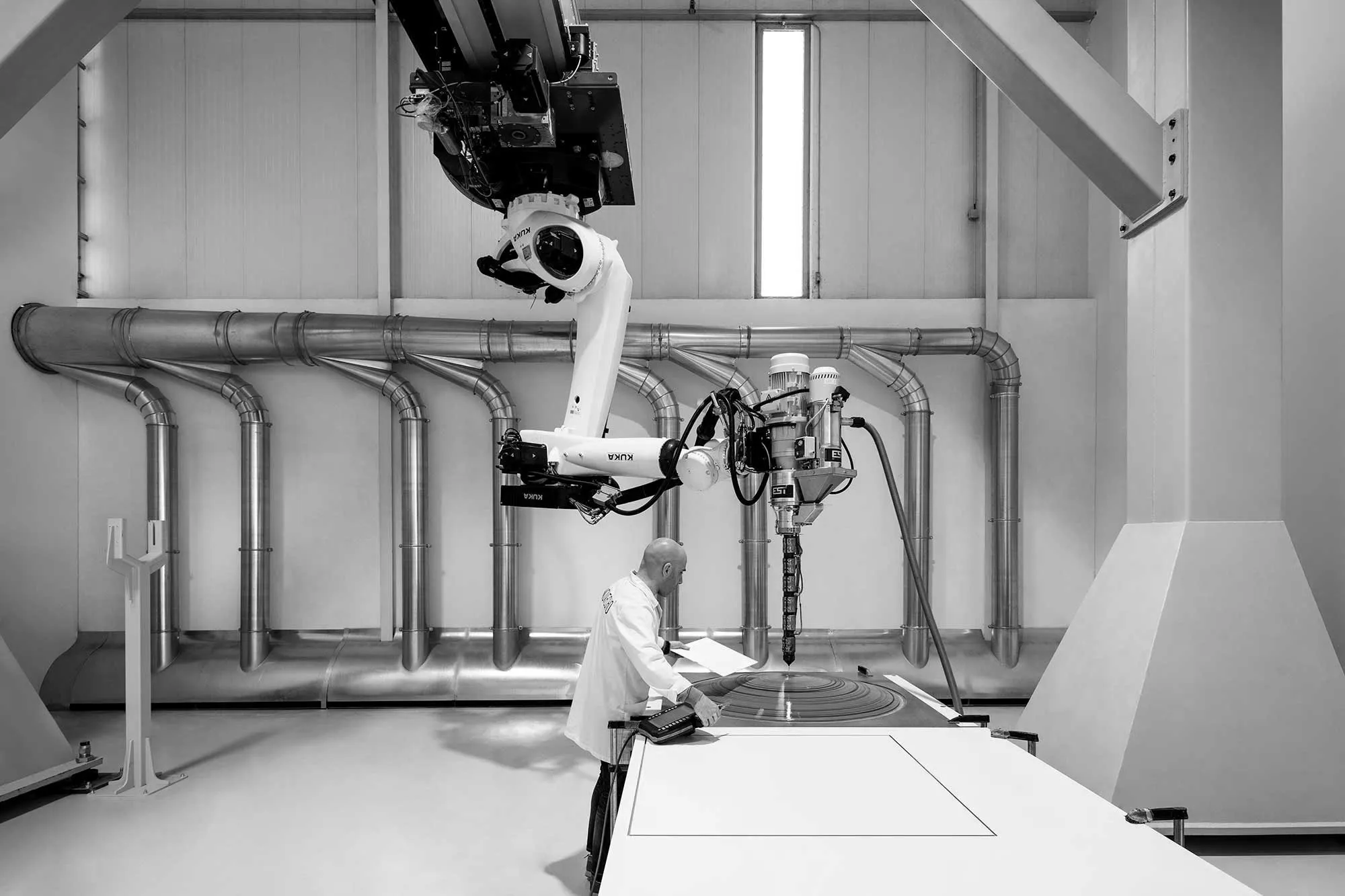 Técnico observa máquina industrial robótica operando em ambiente limpo e moderno.