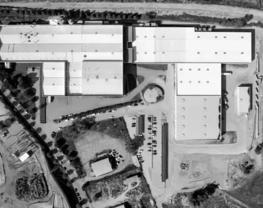 Imagem aérea em preto e branco de um complexo industrial com grandes edifícios e áreas de estacionamento.