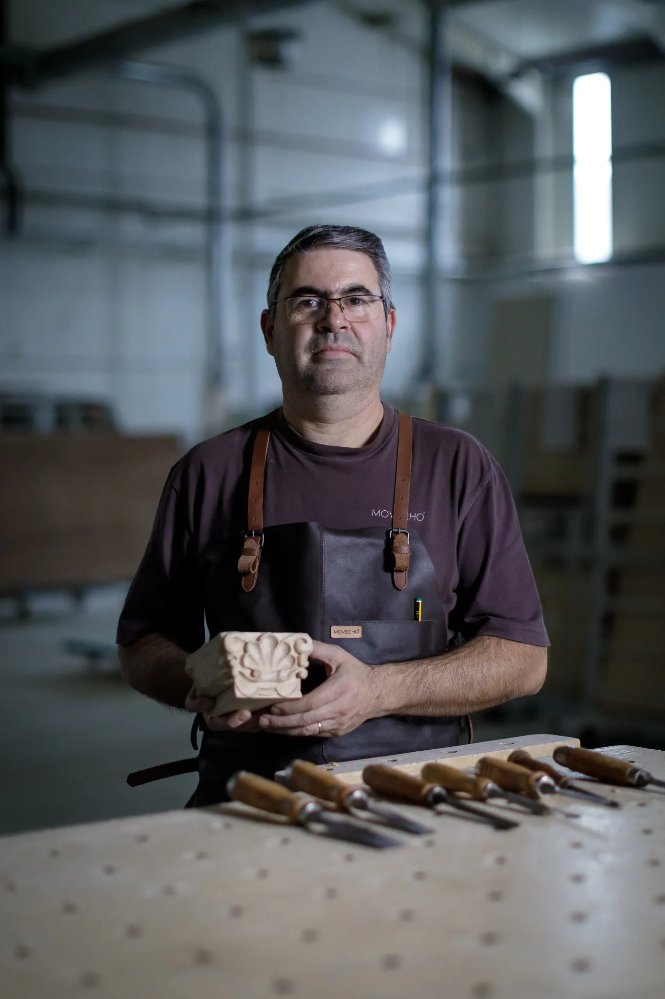 Carpinteiro segurando escultura de madeira decorativa em oficina com ferramentas na mesa.