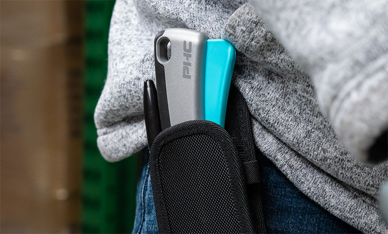 Close-up of a black pouch attached to jeans pocket holding a silver PiiC phone case, blue item, and black pen.