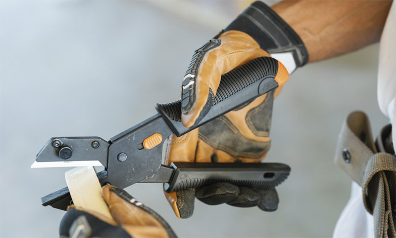 Person wearing work gloves using a black and orange utility knife to cut tape.