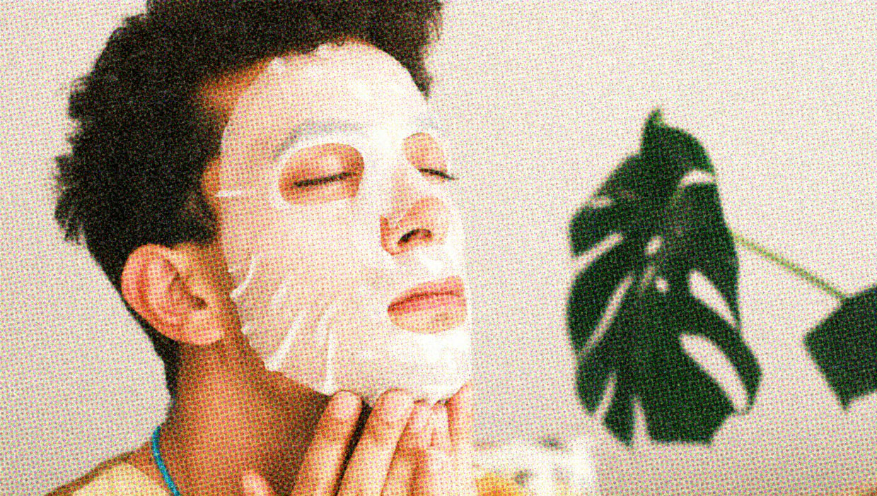 A person wears a sheet mask on their face. Their facial expression is relaxed.