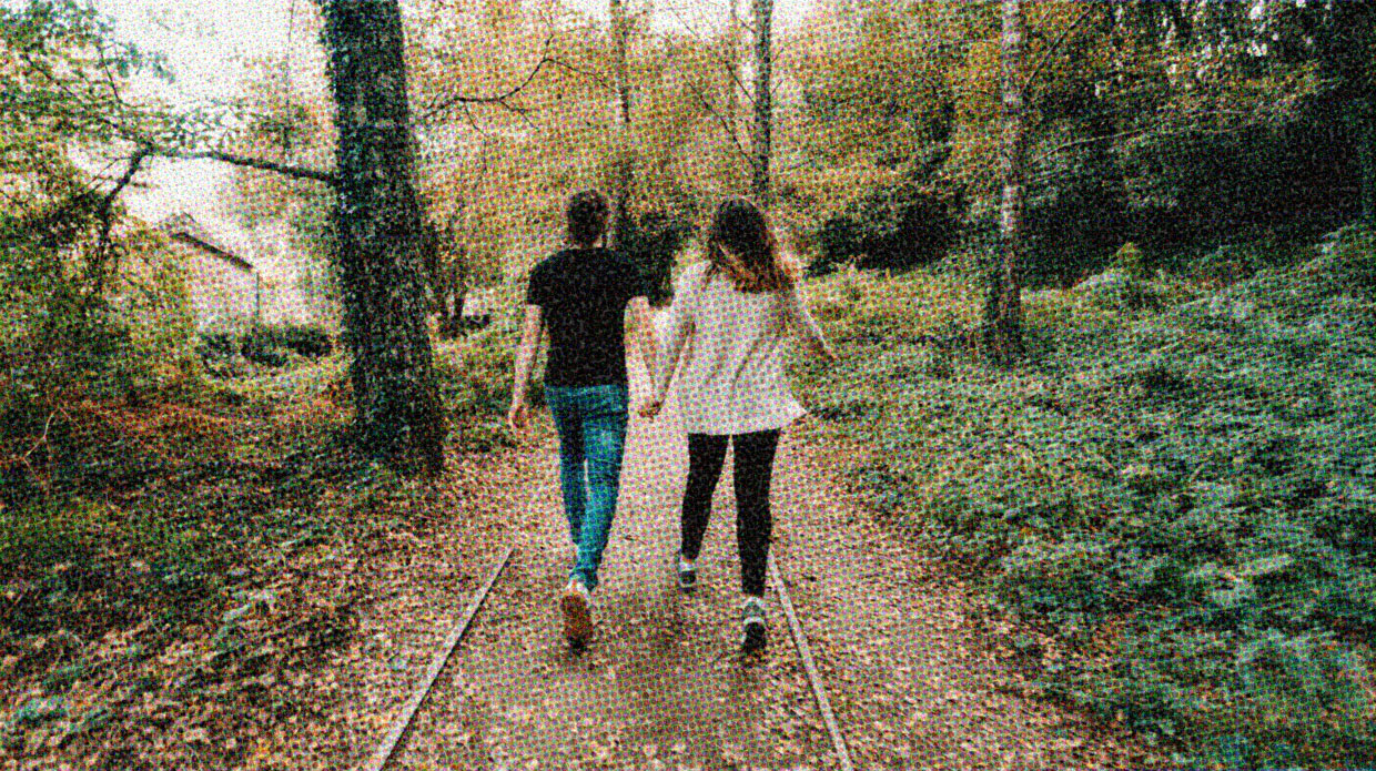 Two people walk along a forest path together, holding hands.
