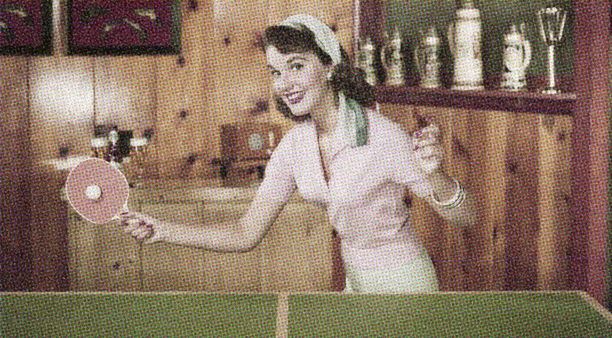 A vintage snap of a woman playing ping-pong. Her paddle is raised and she has a playful, expectant look on her face.