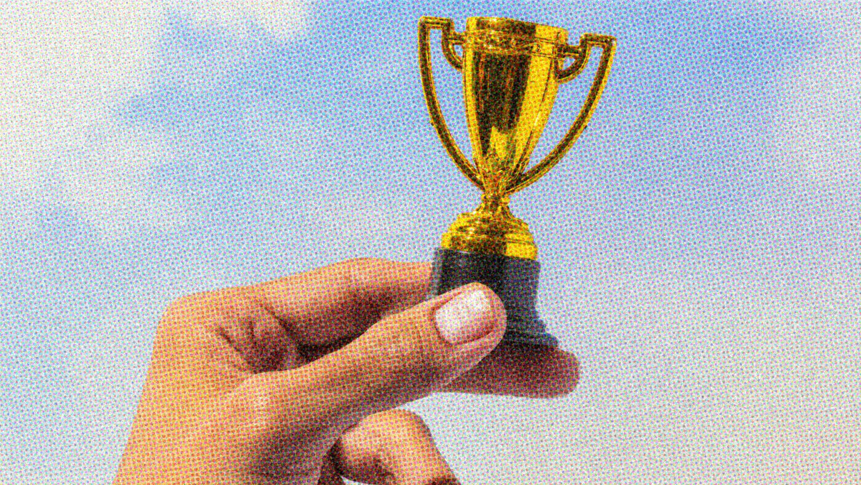 A preson triumphantly holds up a very small, very shiny gold trophy.