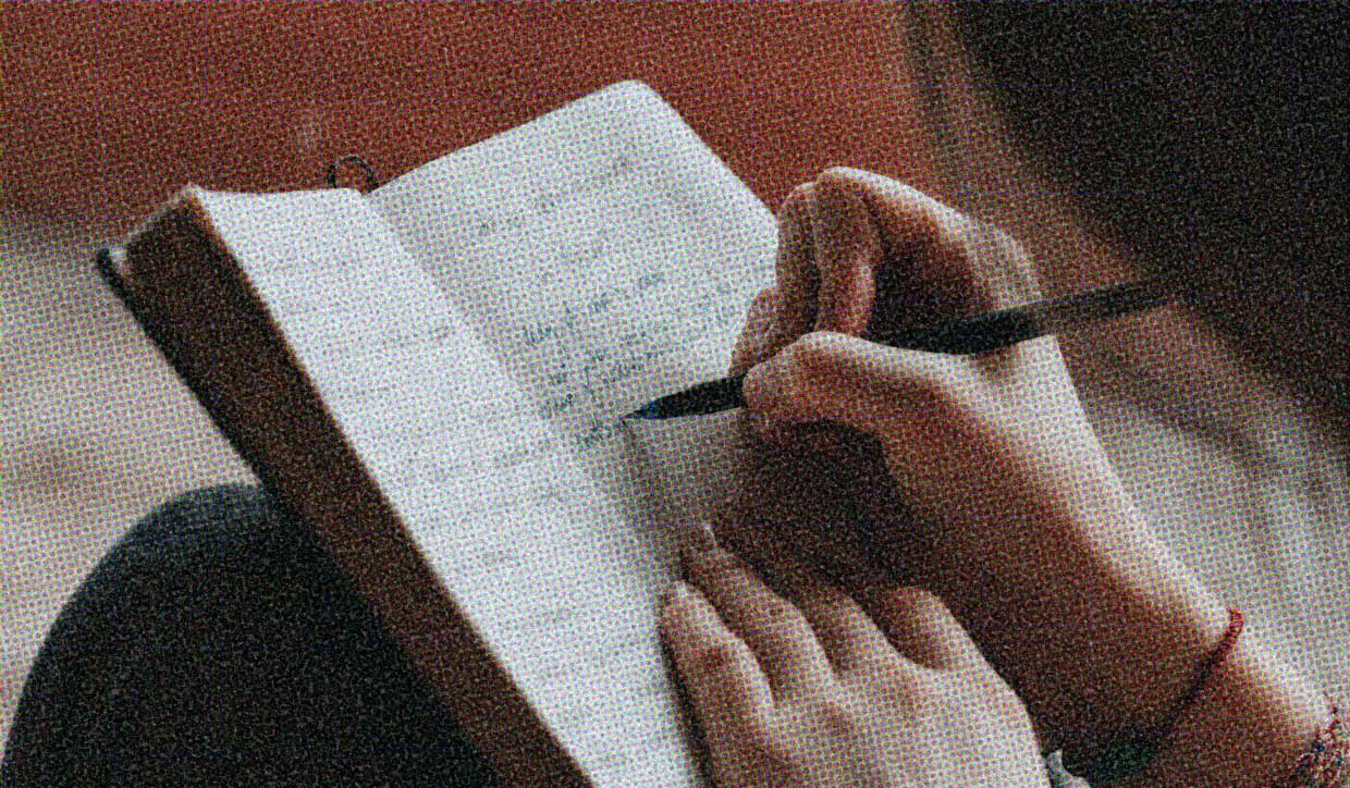 A hand holds a pen, poised over a journal page.