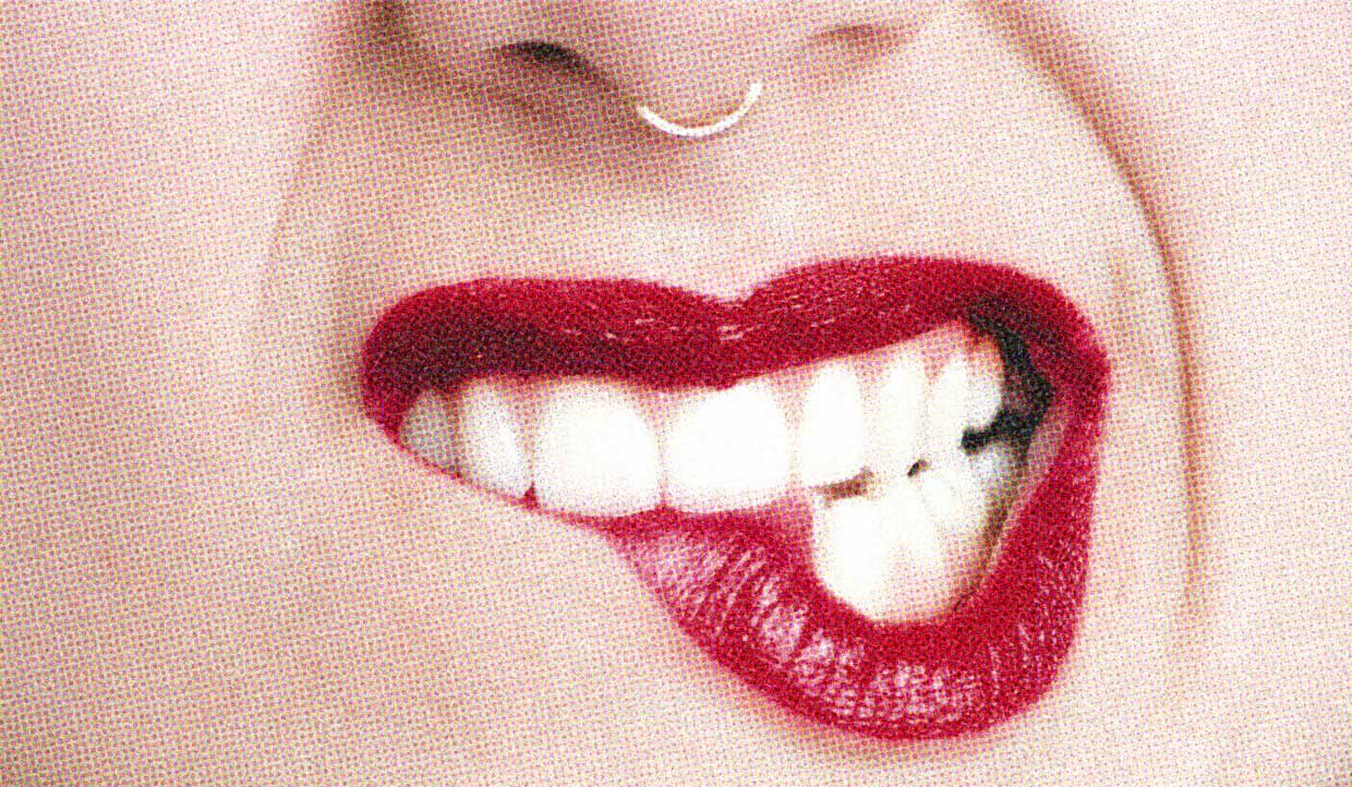 A close-up of a pale-skinned person's face. They have a nose ring and are wearing bright red lipstick. They are biting their lip.