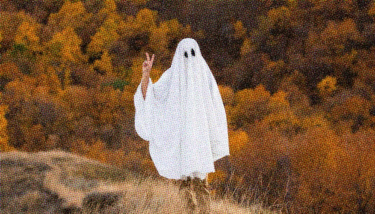 A person wearing a sheet ghost costume gives a peace sign with their fingers. Peacing out, perhaps?