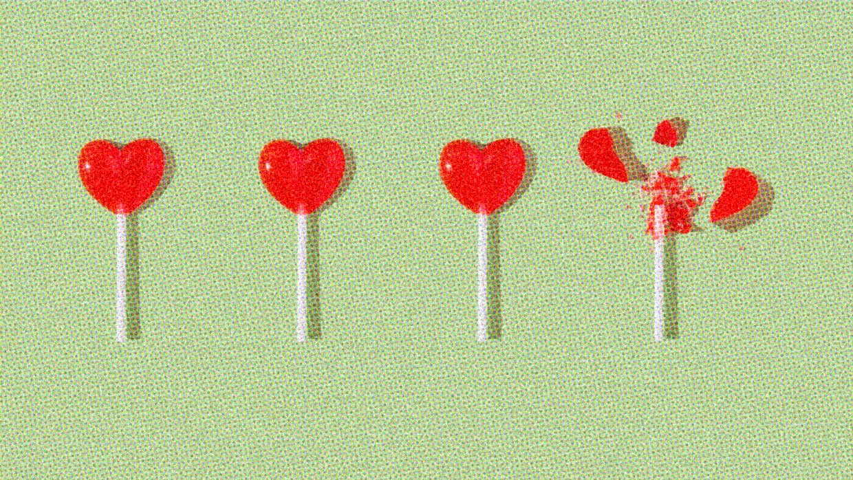 Four red heart-shaped lollipops are on a green background. The lollipop on the far right has been smashed and the heart shape is in pieces.
