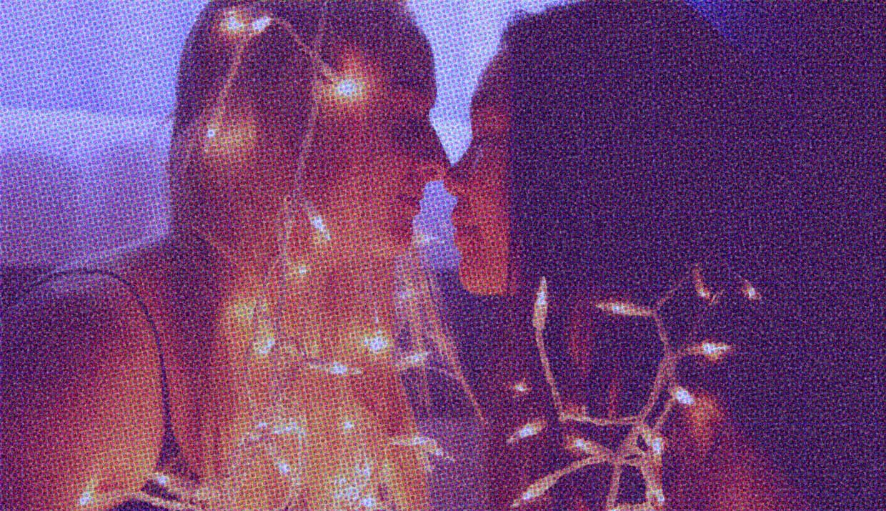 Two people kiss, their faces softly lit by twinkling fairy lights.
