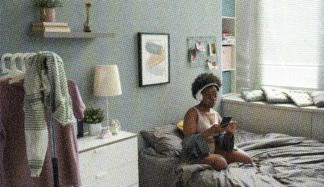 A woman sits on her bed in her bedroom, wearing headphones and vibing. She's not lonely, she's enjoying her alone time in her own space.