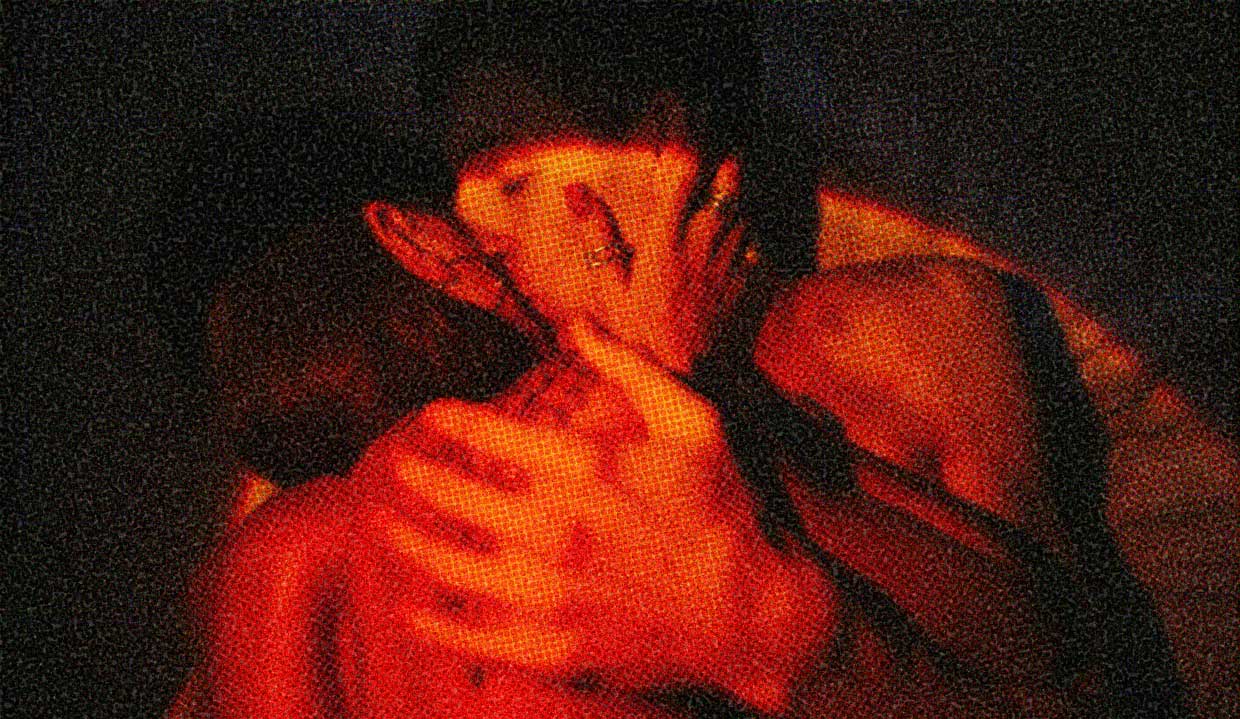 Two people embrace, flooded in unsettling red light.