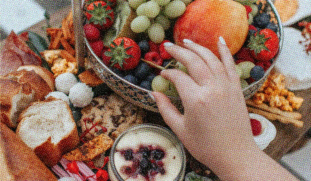 A table laden with delicious food. A hand hovers over the feast, choosing carefully.