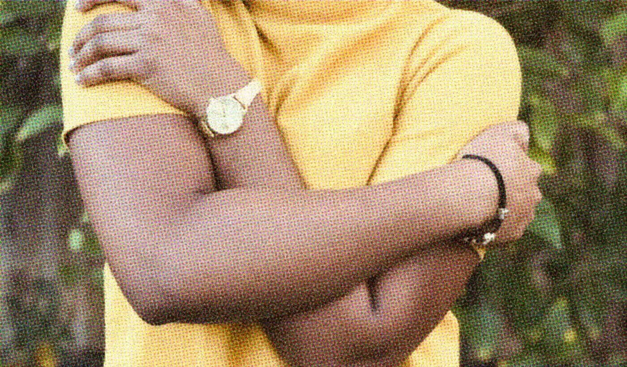 A woman wearing a yellow shirt hugs herself.