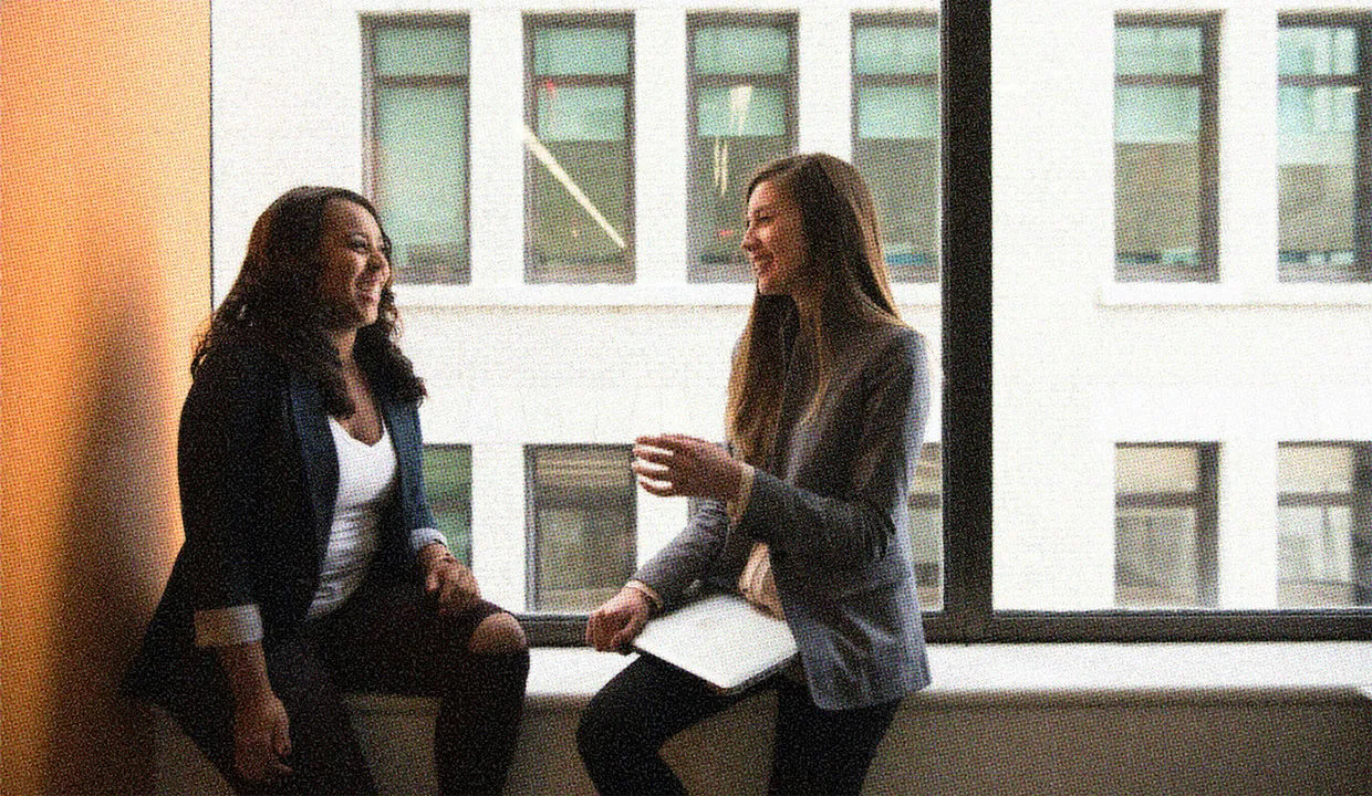 A couple of colleagues laughing together in the corner of an office. 