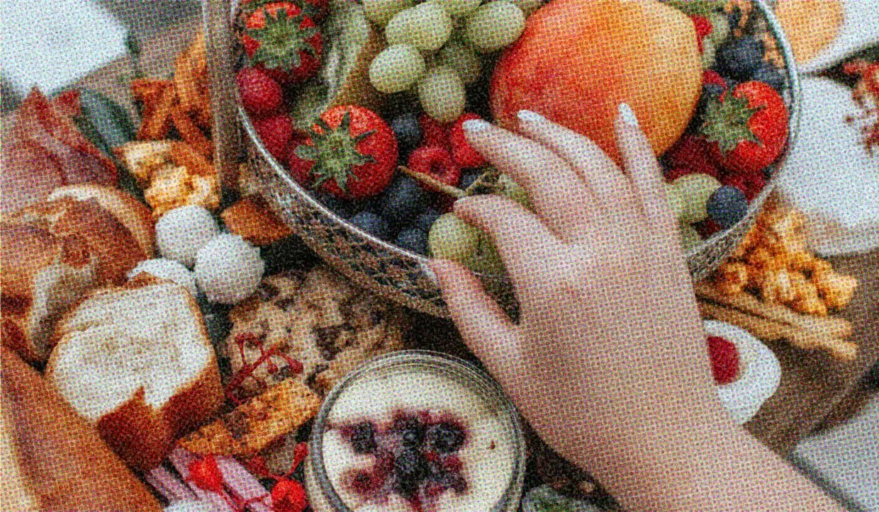 A table laden with delicious food. A hand hovers over the feast, choosing carefully.