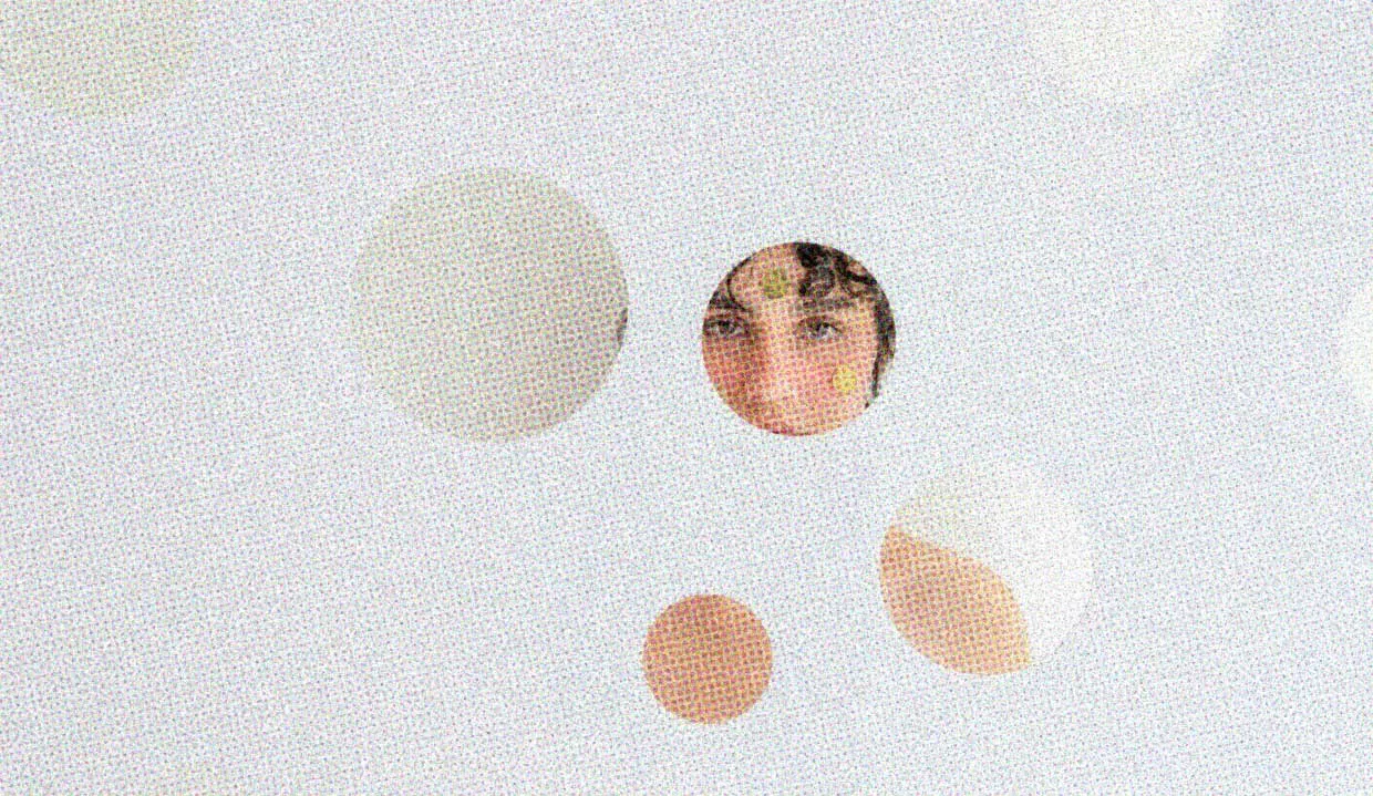 A woman looks at the viewer through a circular cutout in a wall that has many other circular cutouts at different levels.