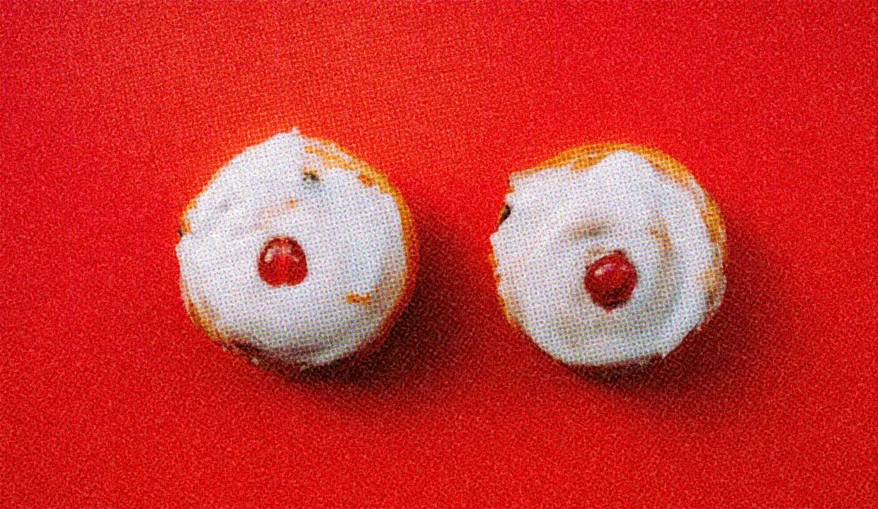 Two donuts with vanilla icing and cherries on top.