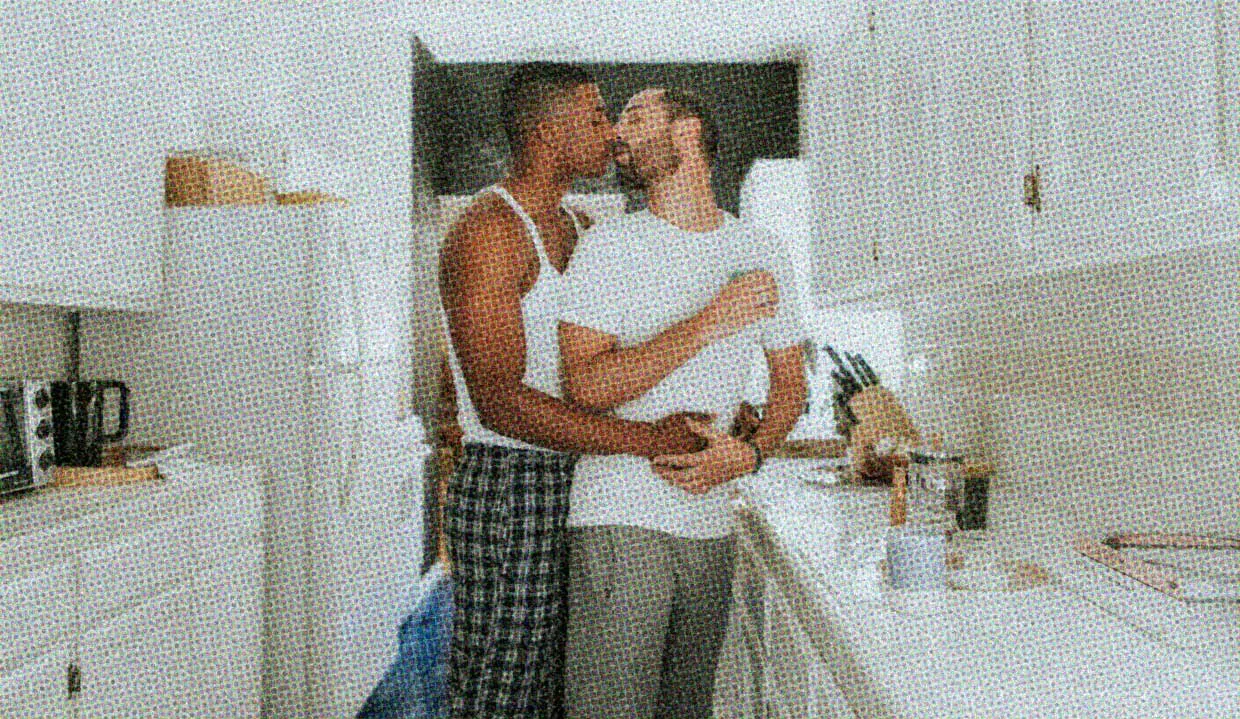 In a pristine white kitchen, two men embrace while preparing coffee.