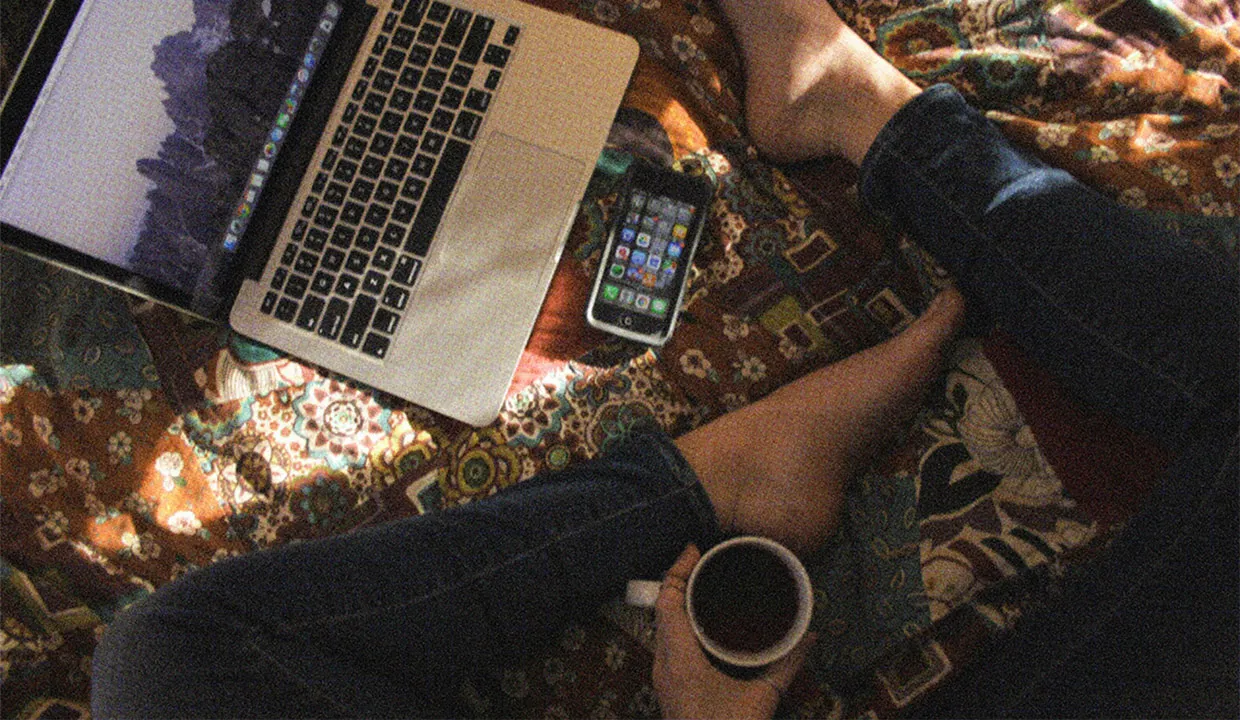 A woman relaxing on her bed with a coffee, editing her dating profile.