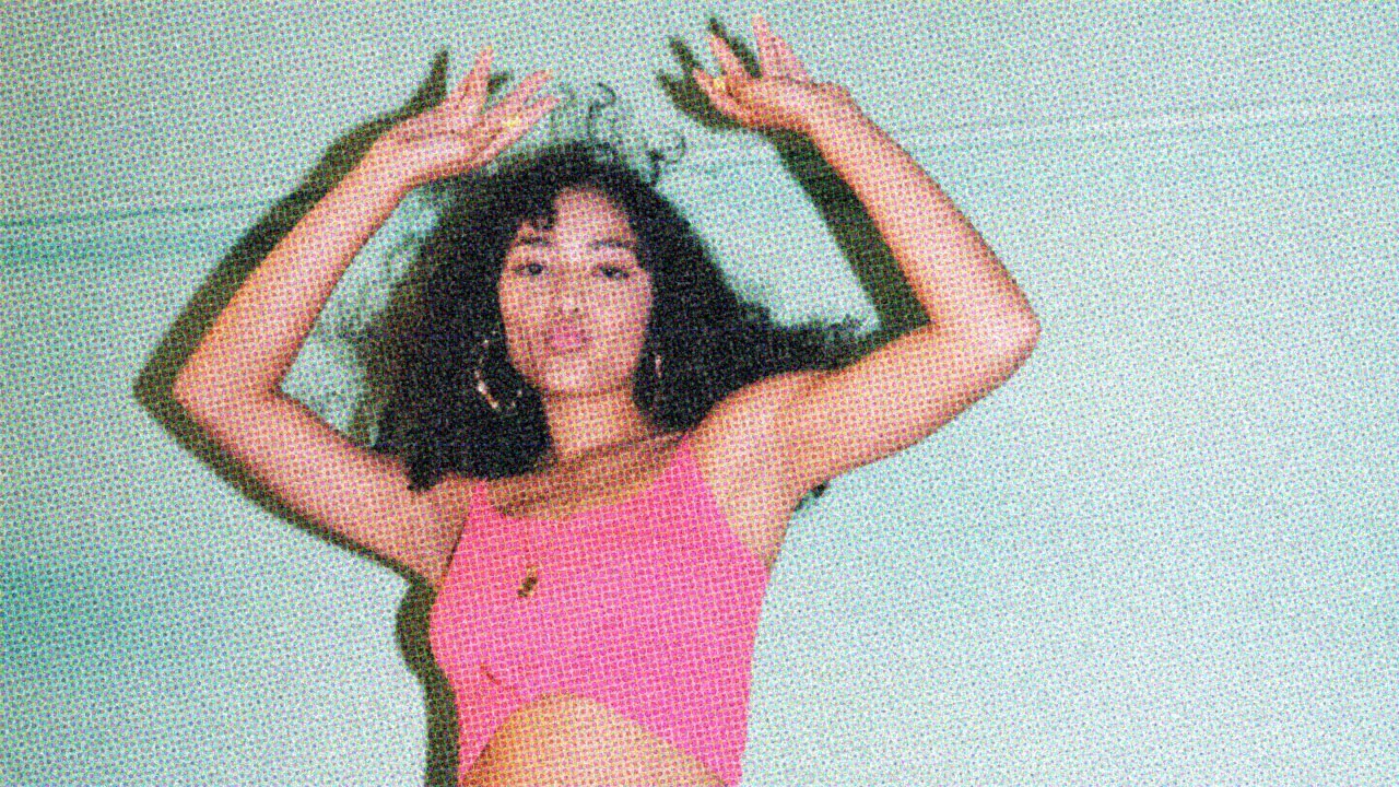 A confident woman dancing in front of a pale green backdrop.