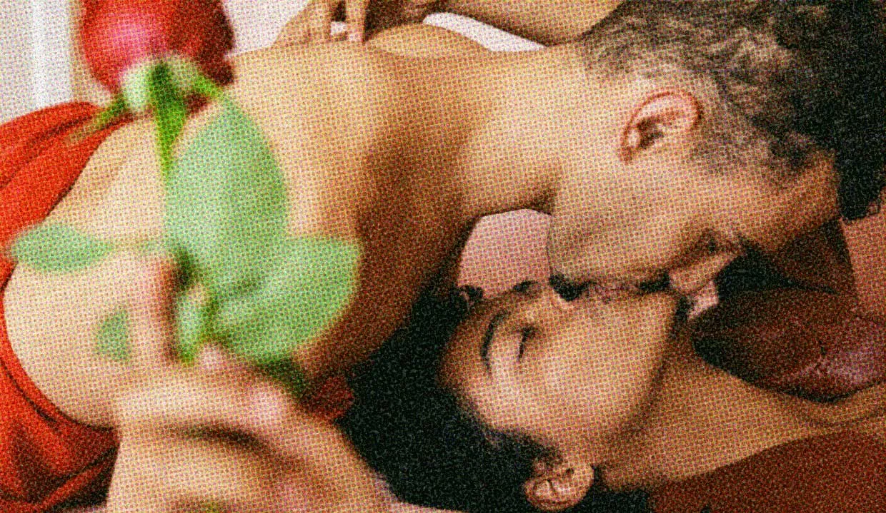 Two people kiss. One is holding a red rose.
